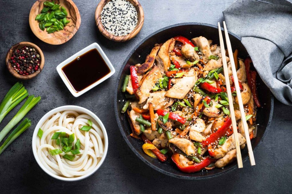 Chicken Stir fry, udon noodles and soy sause on black stone table. Traditional asian food. Top view.