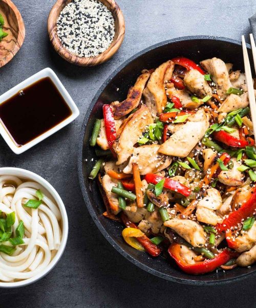 Chicken Stir fry, udon noodles and soy sause on black stone table. Traditional asian food. Top view.